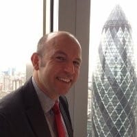 Kevin Brown smiles in front of a window, with the Gherkin skyscraper visible behind him.