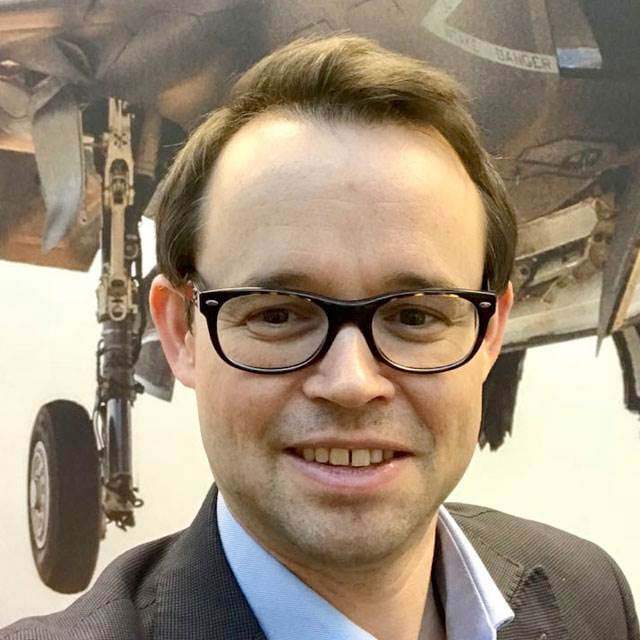 Dickon Skinner smiles in front of an image of an aircraft.