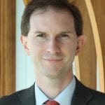 James Robey in grey suit and shirt and tie, smiles into the camera