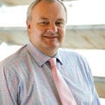 Richard Ellis in blue shirt and pink tie smiles