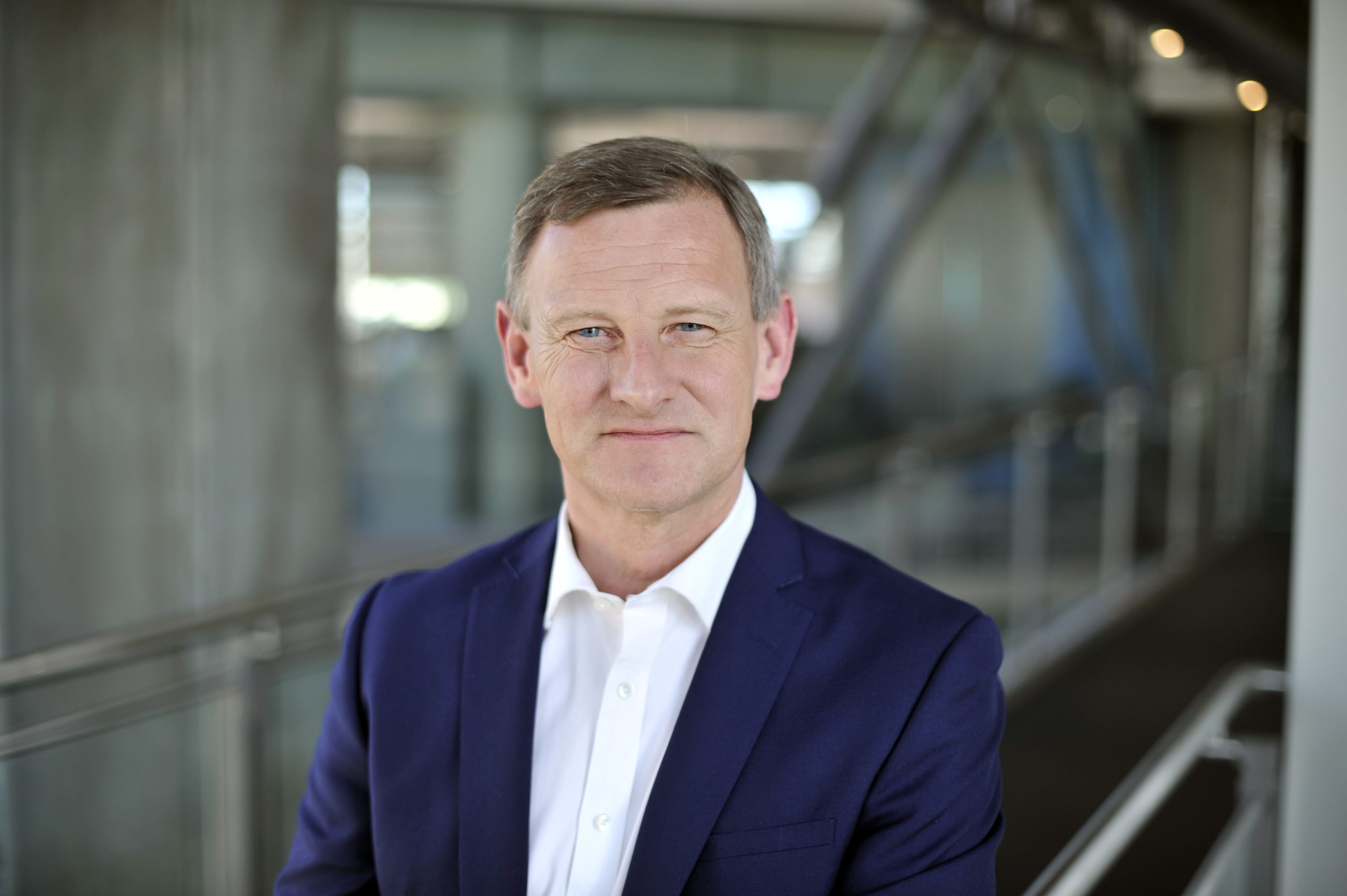 Steve Rowe in a navy suit and a white shirt looks at the camera