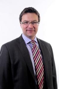 Richard Warneford in suit and striped tie looks at the camera