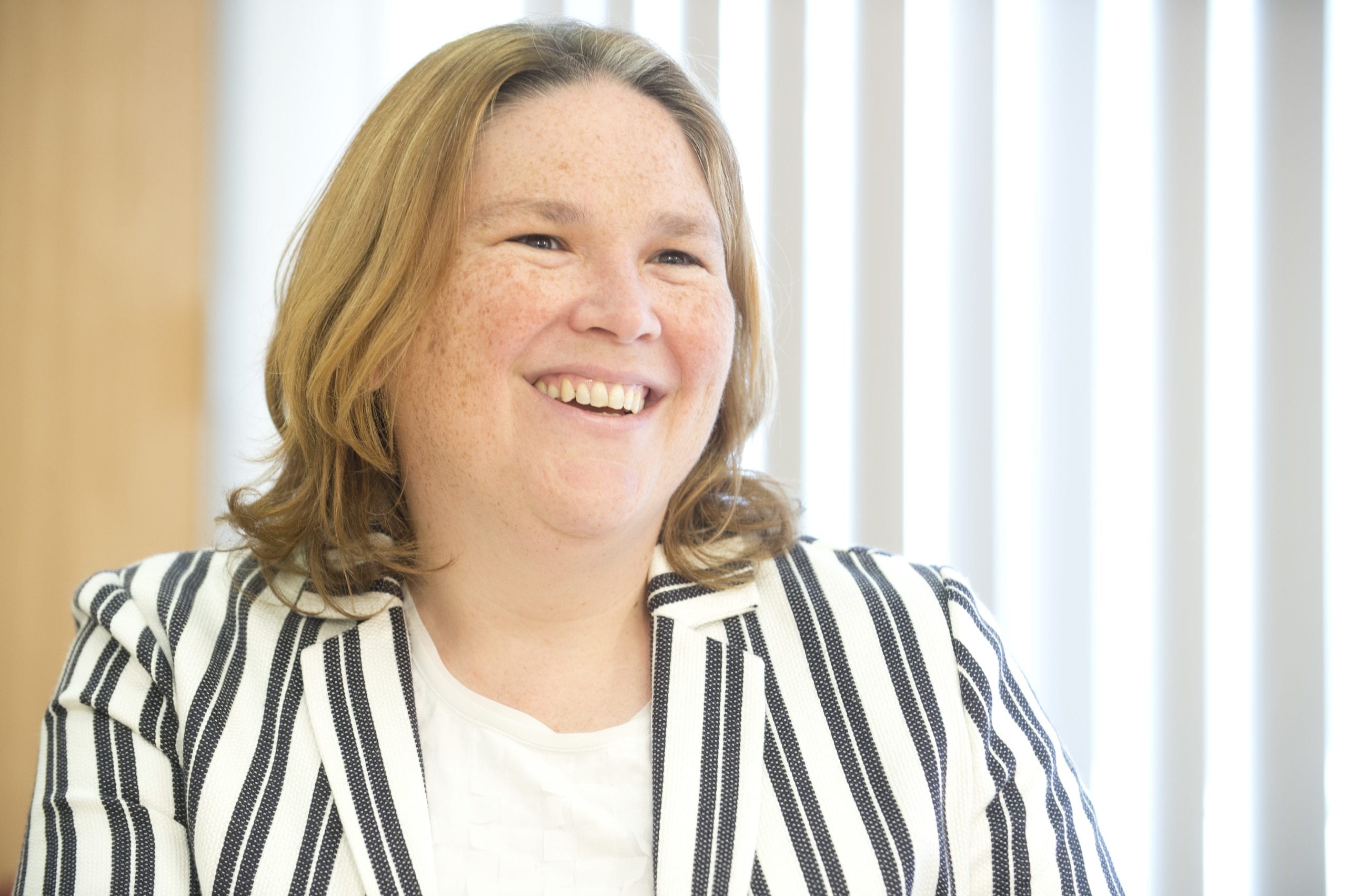 Paula Swain in a striped jacket smiles off camera